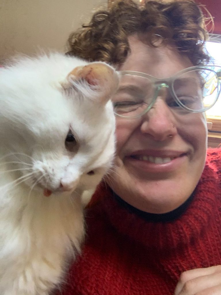 curly haired person and their fluffy white cat loving on them because pets don't need to do anything to deserve to be loved